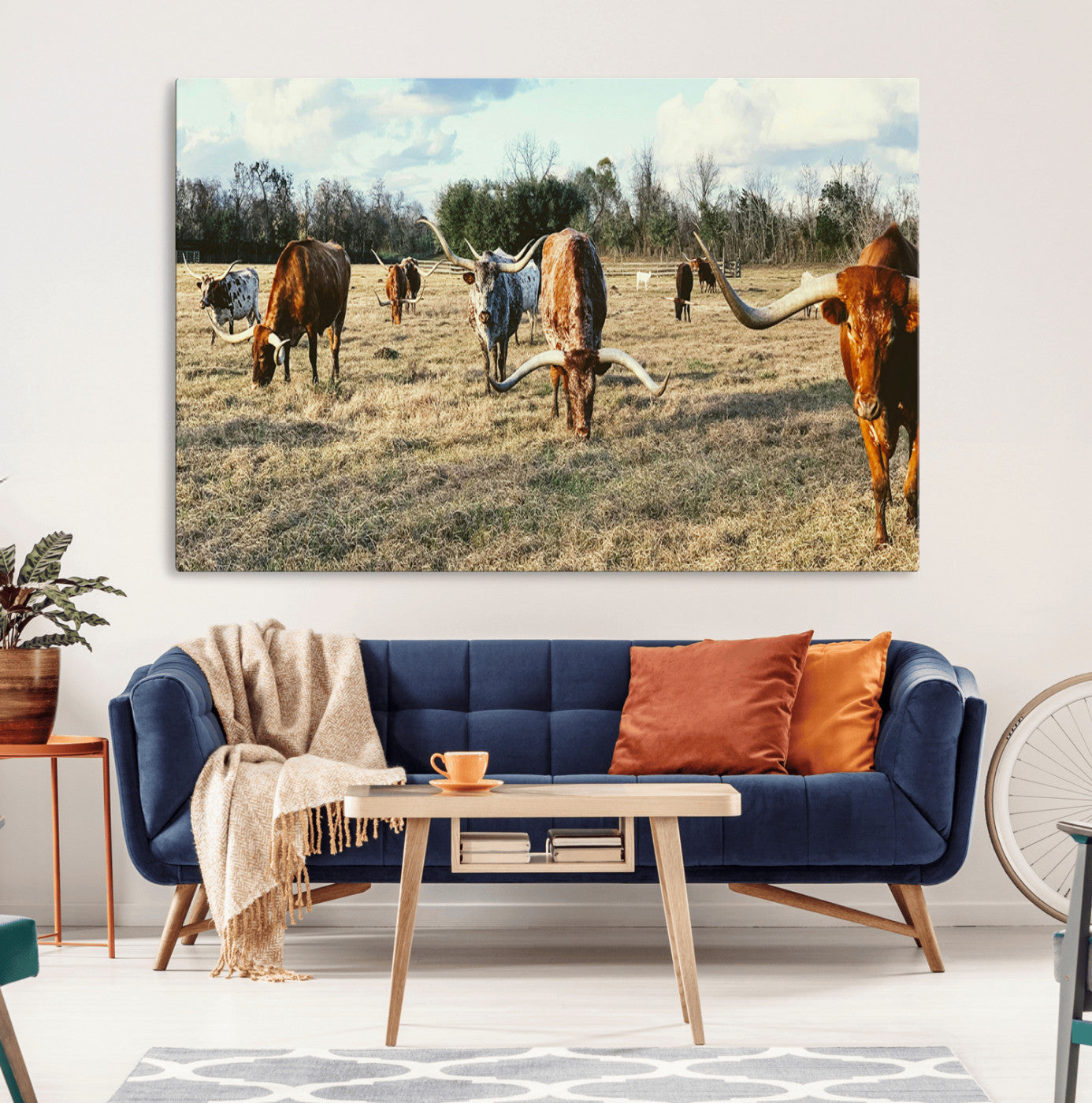 A herd of Texas Longhorn cattle grazing in an open field under a partly cloudy sky, capturing a rustic and Western ranch aesthetic.