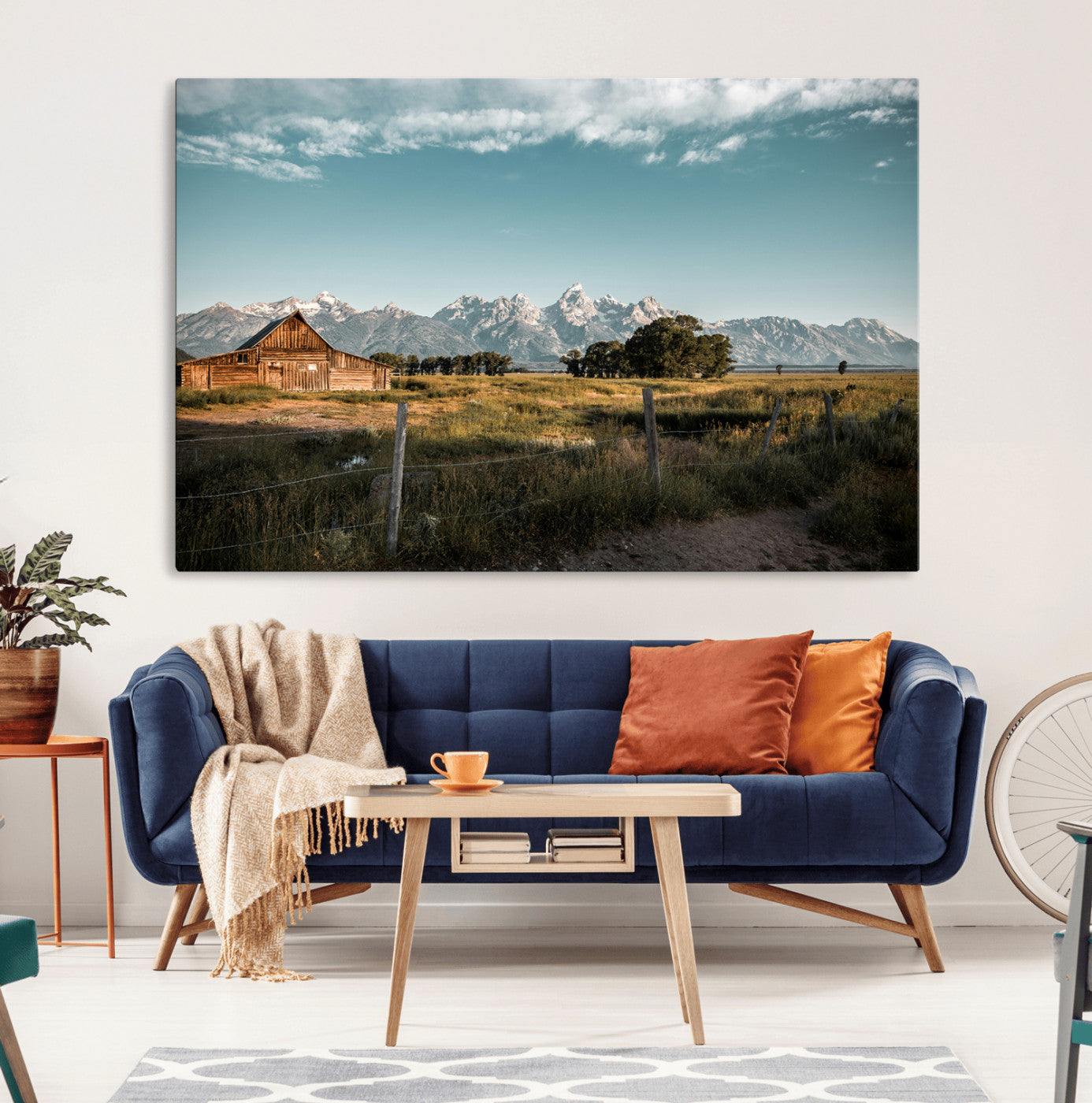 A rustic farmhouse with a wooden barn set against majestic mountain peaks under a soft blue sky, evoking peaceful countryside charm.