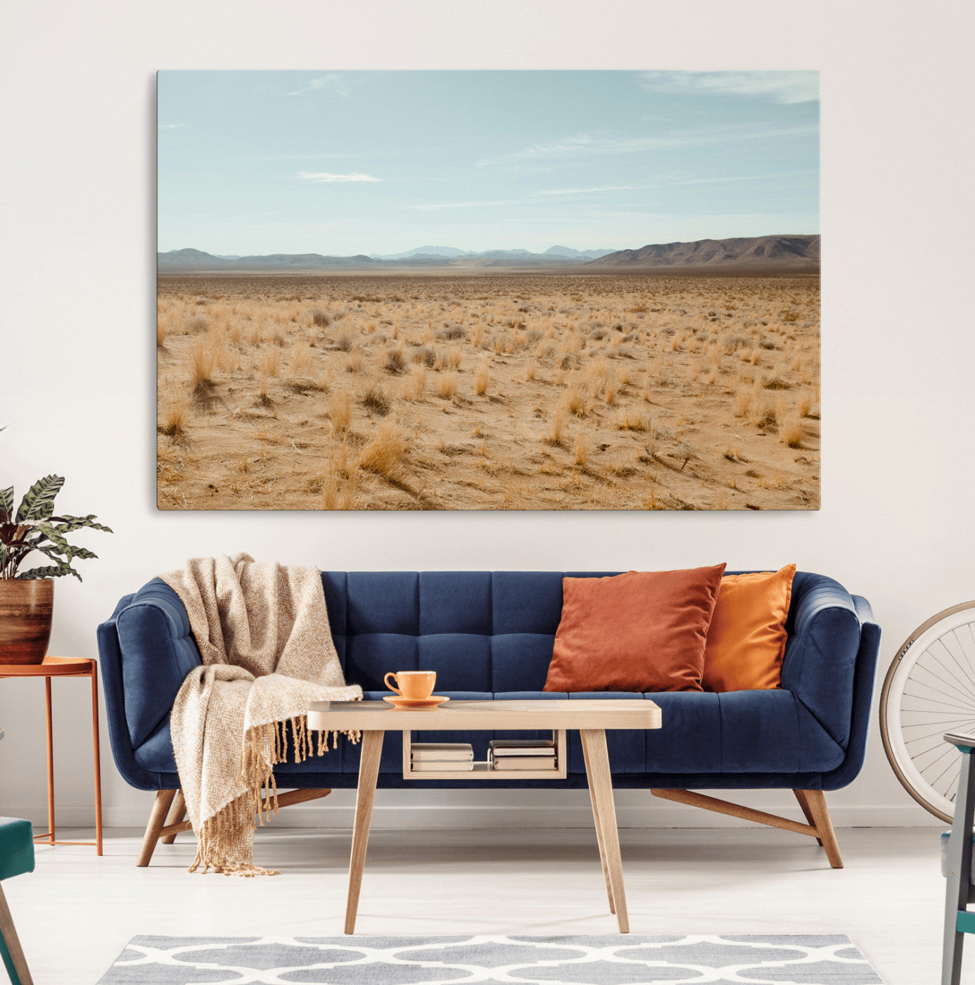 Expansive desert landscape with scattered dry grass and distant mountain range under a pale blue sky – Wall Art Canvas Print.