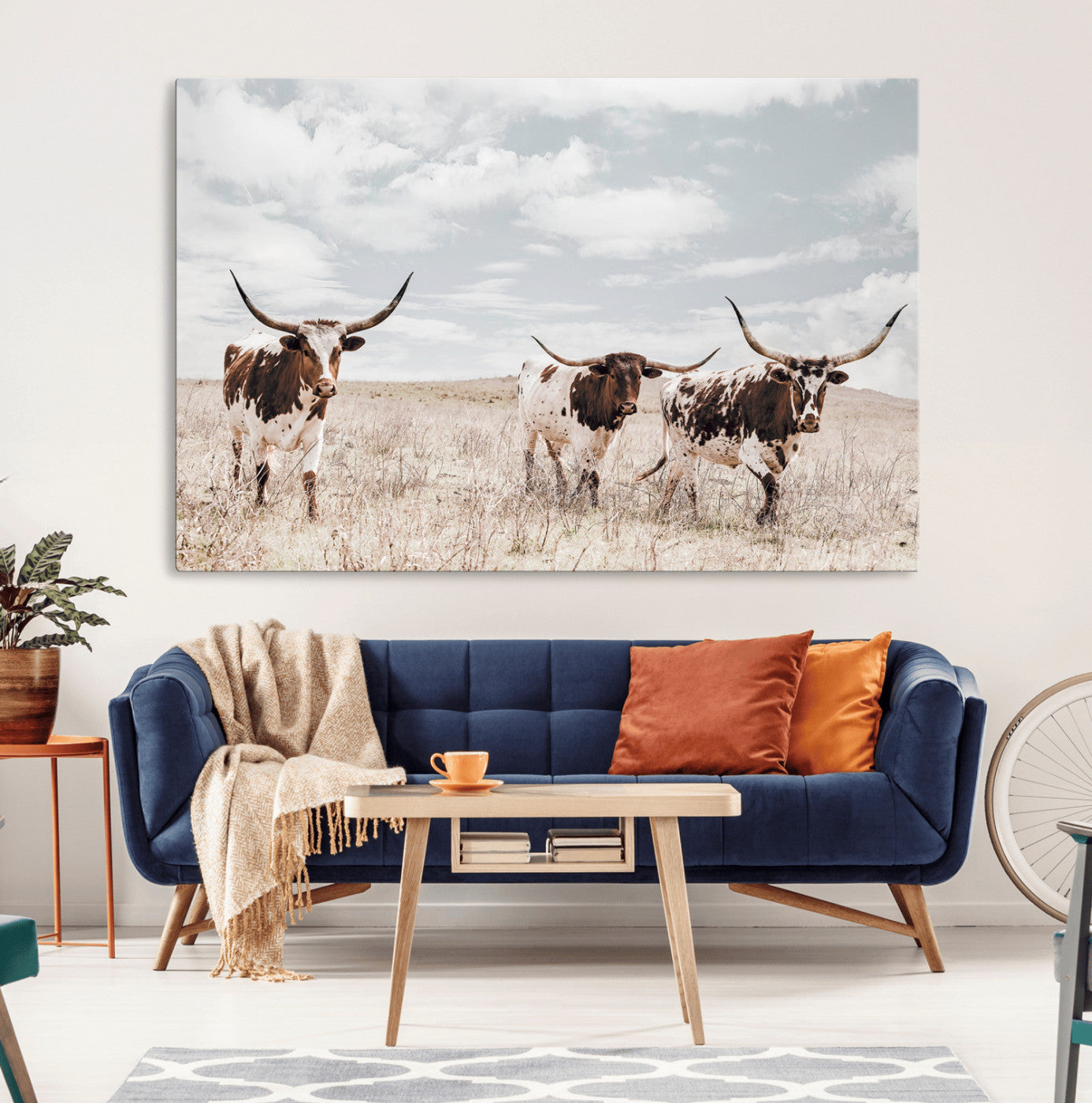 Three Texas Longhorn cattle walking through a dry grassy field under a partly cloudy sky.