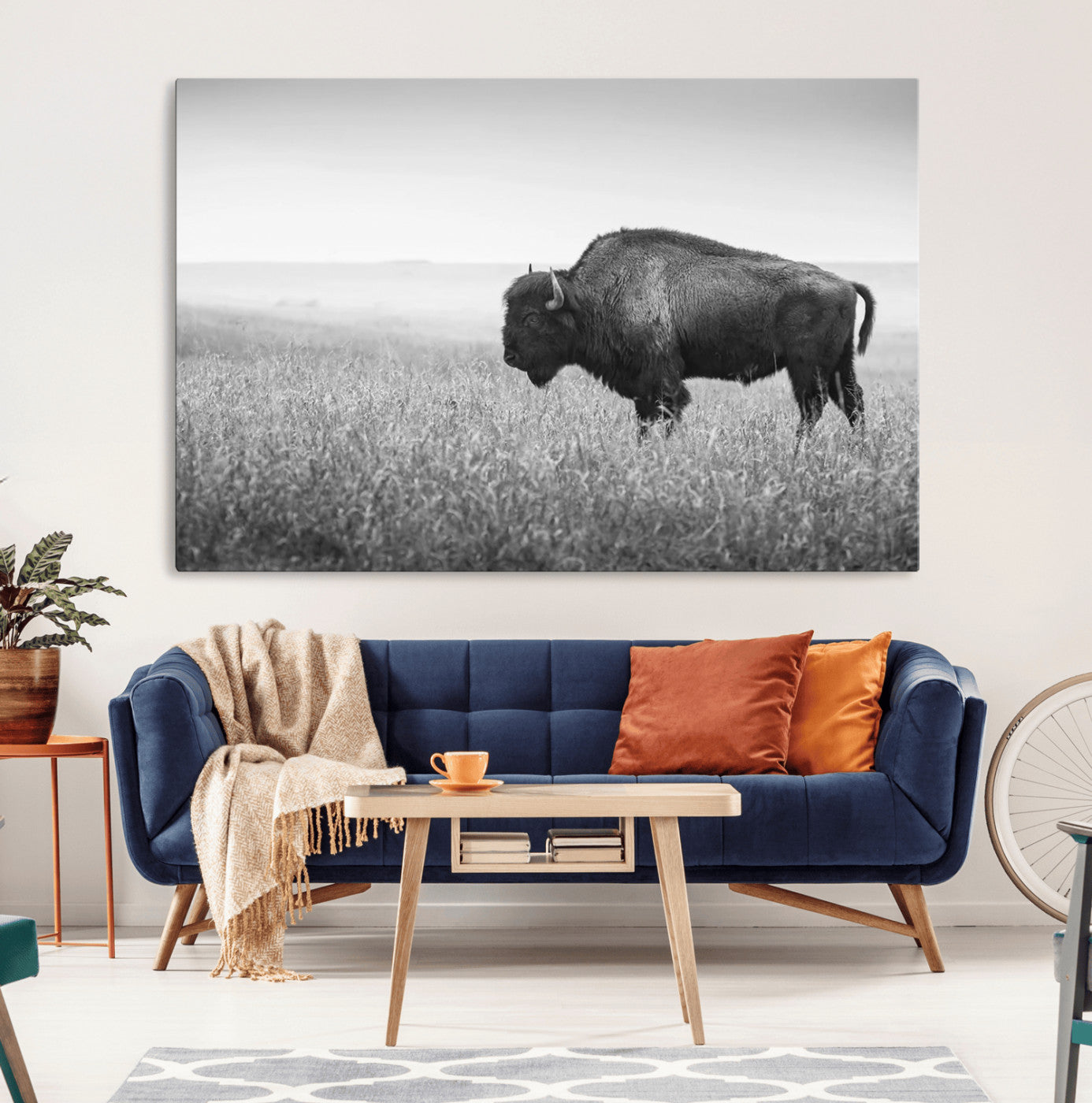"Black and white image of a bison grazing in a vast field under an overcast sky."
