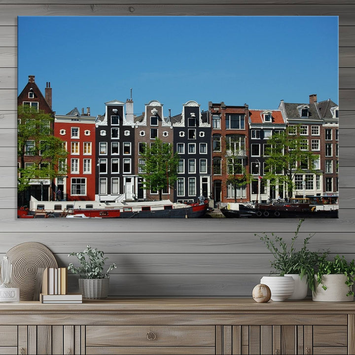 The Amsterdam City Wall Art Canvas Print showcases colorful traditional canal houses and boats set against a clear blue sky.