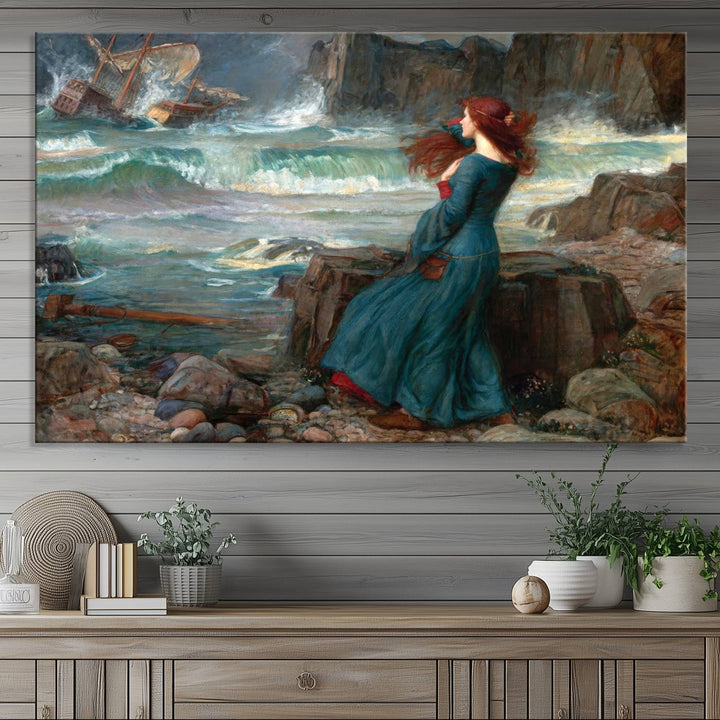 The Miranda by the Shore Wall Art Canvas Print depicts a woman in a blue dress standing by the sea, watching a shipwreck.