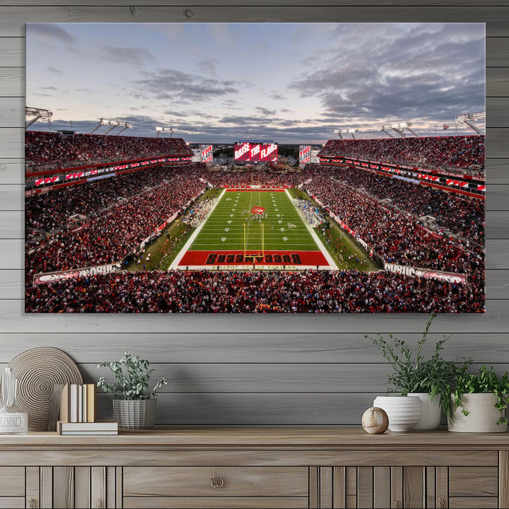 The wall art captures a stunning scene of Raymond James Stadium bathed in the warm hues of sunset. The sky, filled with clouds, provides a dramatic contrast to the vibrant lighting on the field, encapsulating the dynamic energy of a football game.