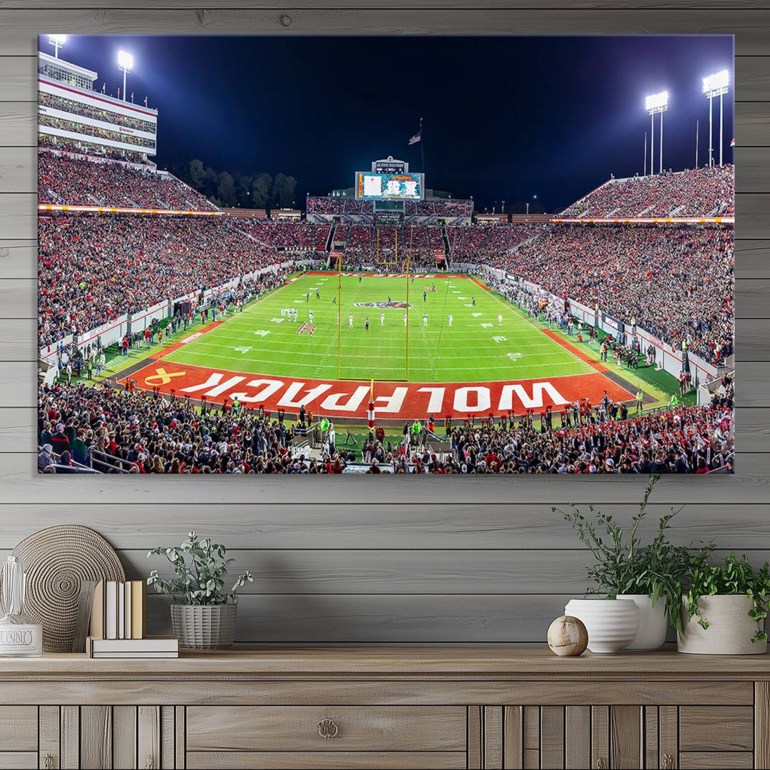 A NC State Wolfpack Football Team print of Carter-Finley Stadium at night features WOLFPACK illuminated brightly in the end zone grass.