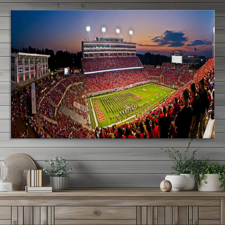 A print of a bustling Carter-Finley Stadium at dusk, featuring fans and a band, captures the essence of NC State Wolfpack football.