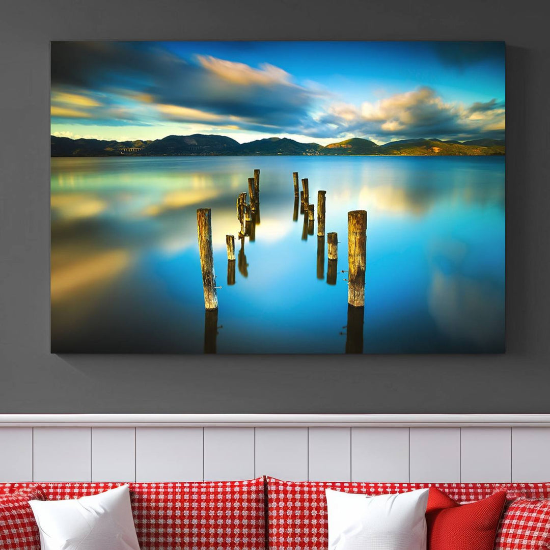 A triptych of a serene lake scene with old wooden pillars, blue sky, and clouds casts a coastal ambiance. The Sea Ocean Sunset Beach Wall Art Canvas Print reflects the soothing nature of the ocean.