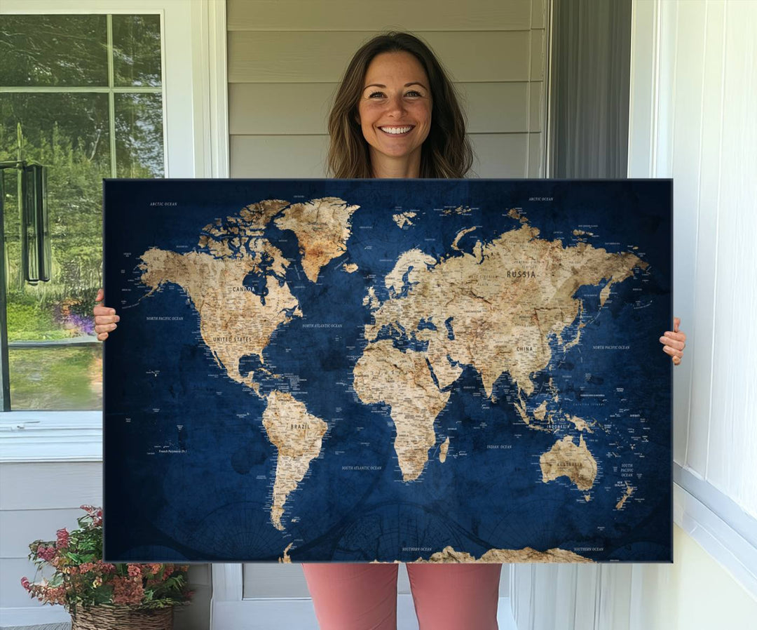 A large framed world map canvas print features beige landmasses set against a grunge-stained deep blue ocean background, creating an intriguing piece of wall art.