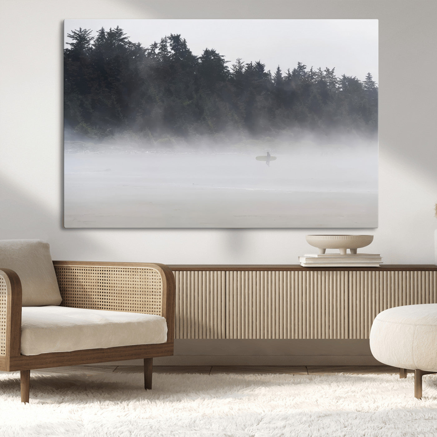 A lone surfer carrying a board through a misty shoreline, surrounded by dense trees and fog, creating a peaceful and mysterious coastal scene.