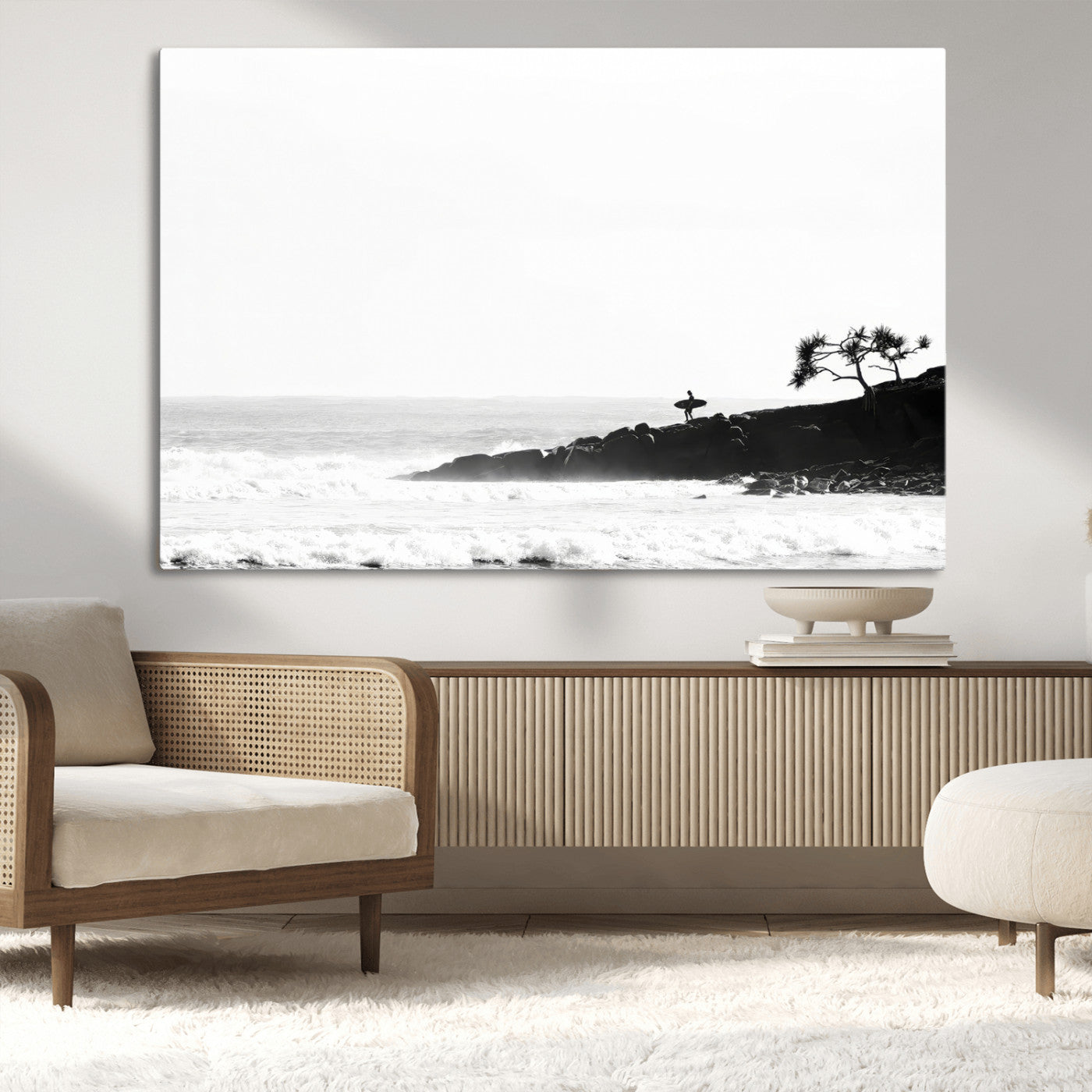 Black and white photo of a surfer standing on rocky cliffs, gazing at the waves, embodying the spirit of adventure and solitude.