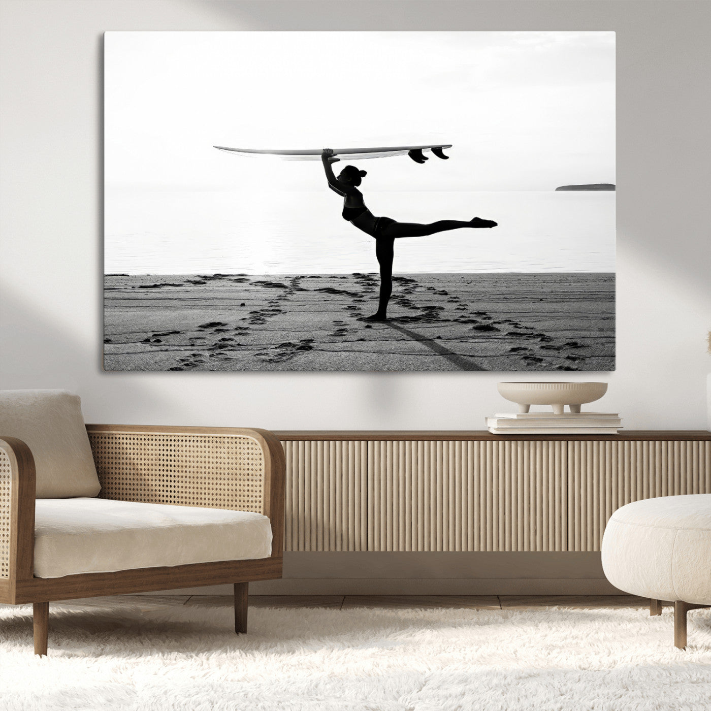 A woman balances a surfboard on her head while striking a yoga pose on the beach, silhouetted against a calm ocean horizon.