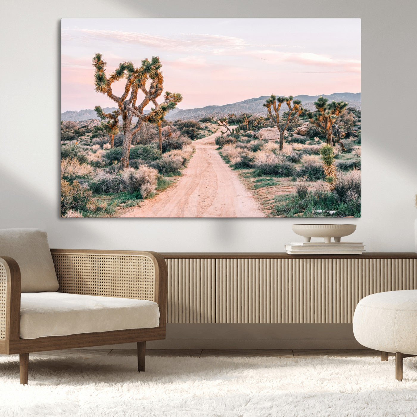 A dusty road winding through Joshua Tree National Park, framed by iconic twisted trees and warm desert tones under a soft pastel sky.