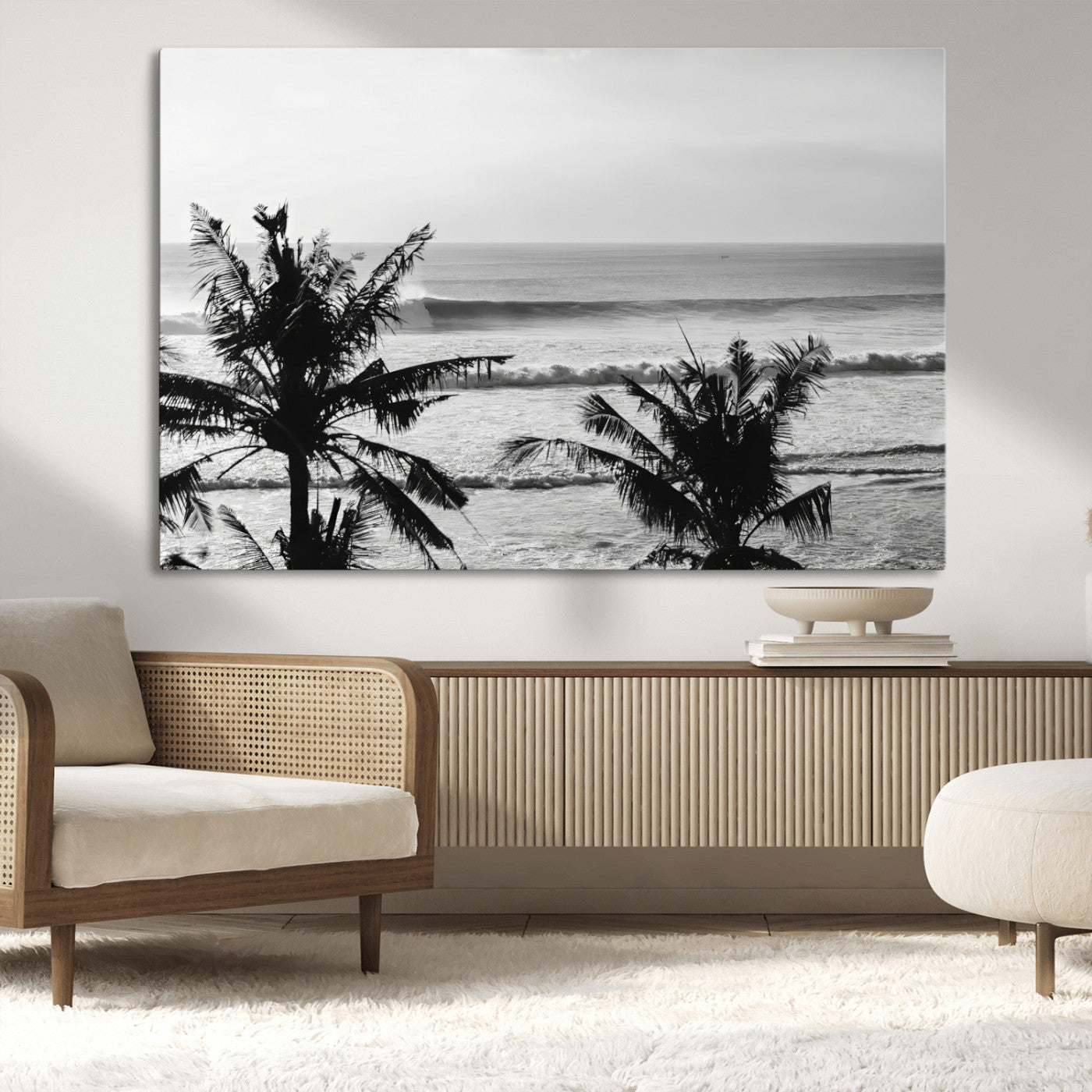 Black and white view of ocean waves crashing on a tropical coastline, framed by silhouetted palm trees under a vast, open sky.
