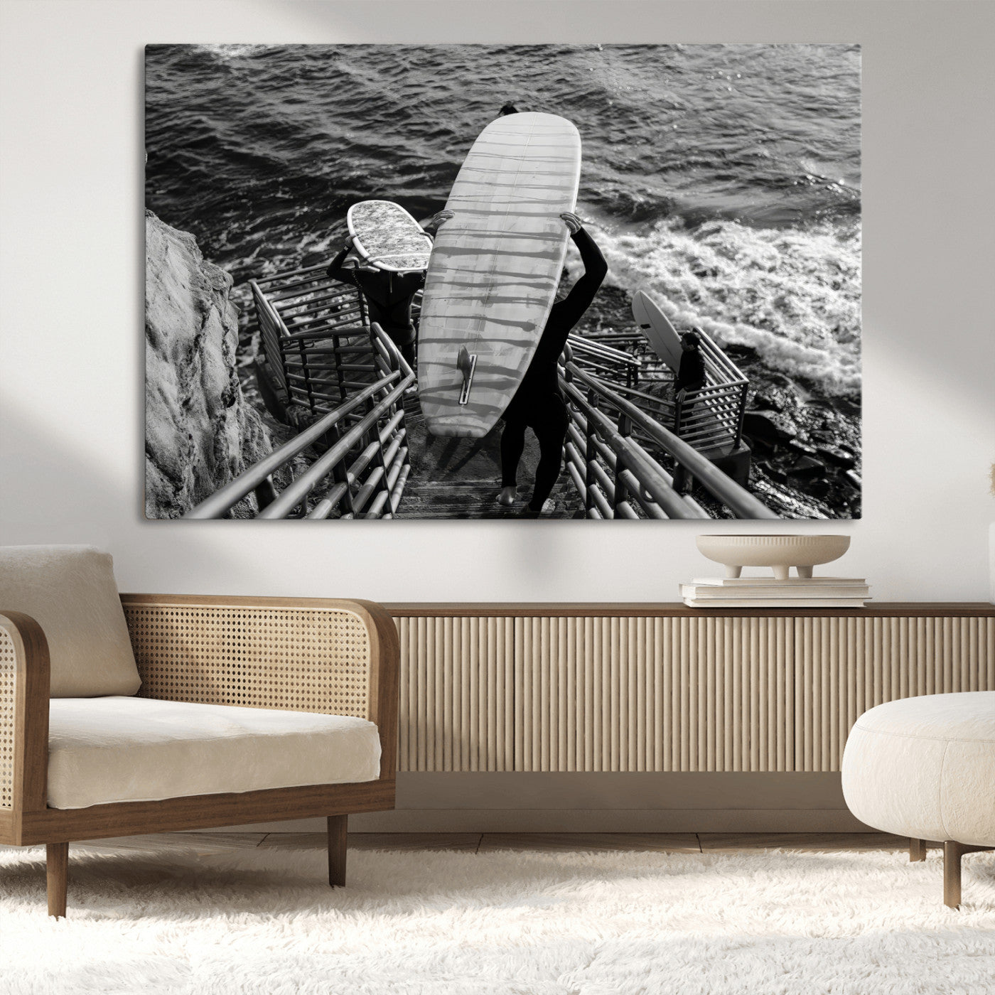 Black and white photo of surfers carrying boards down a rugged cliffside stairway, capturing a bold and adventurous coastal scene.