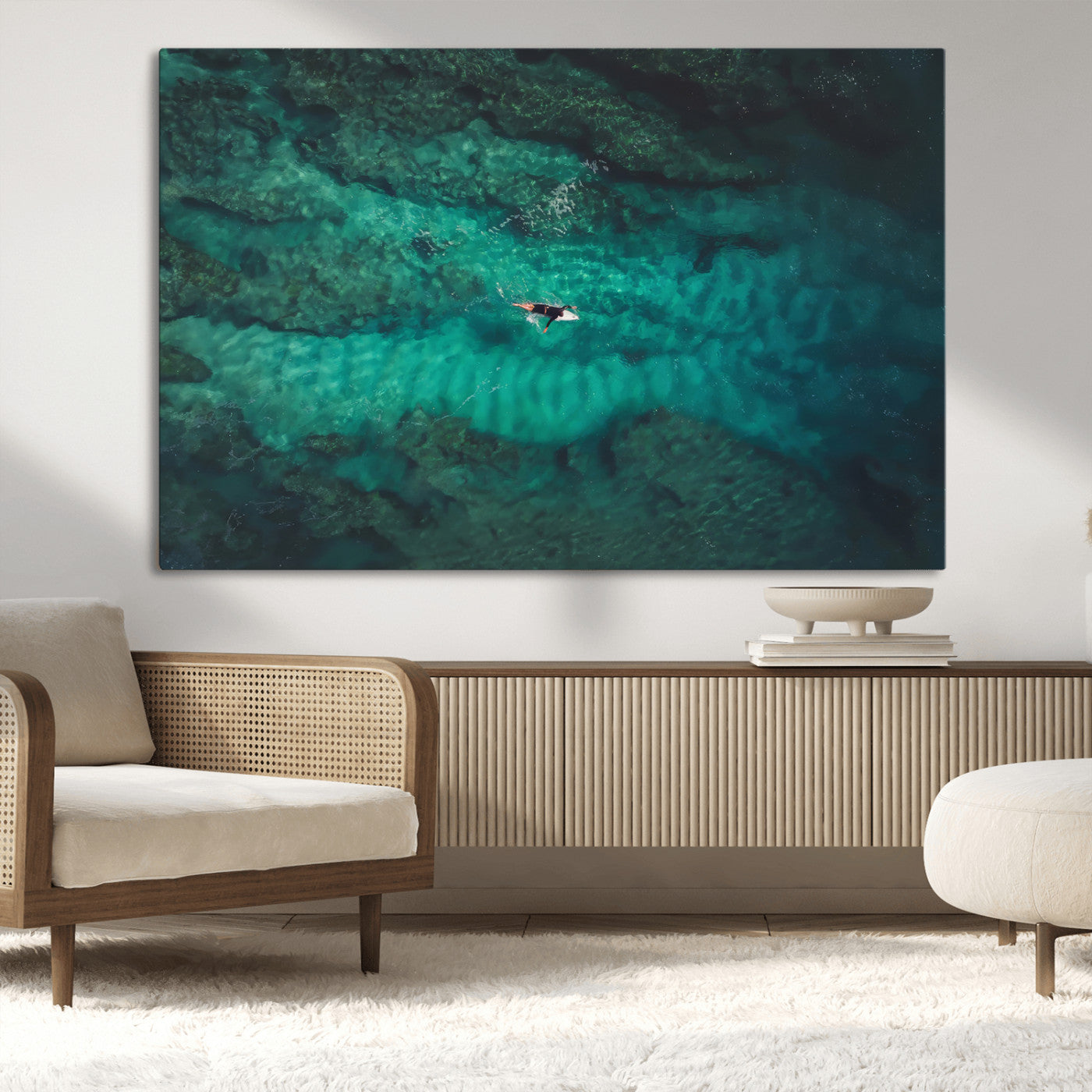 An aerial view of a solo surfer paddling through crystal-clear turquoise waters over a sunlit reef, capturing the beauty and serenity of open water surfing.