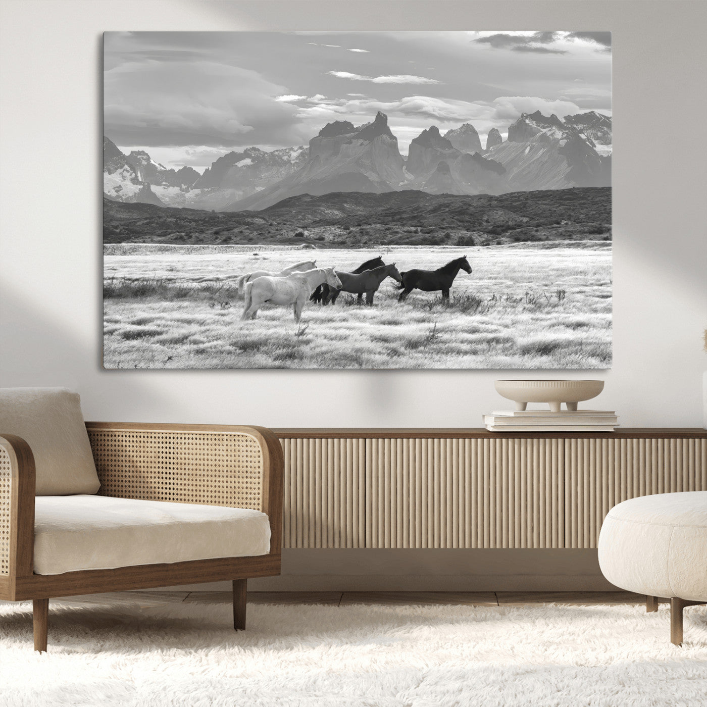 A black and white landscape of wild horses grazing in a vast grassland with towering mountains in the background, creating a moody and rustic western aesthetic.