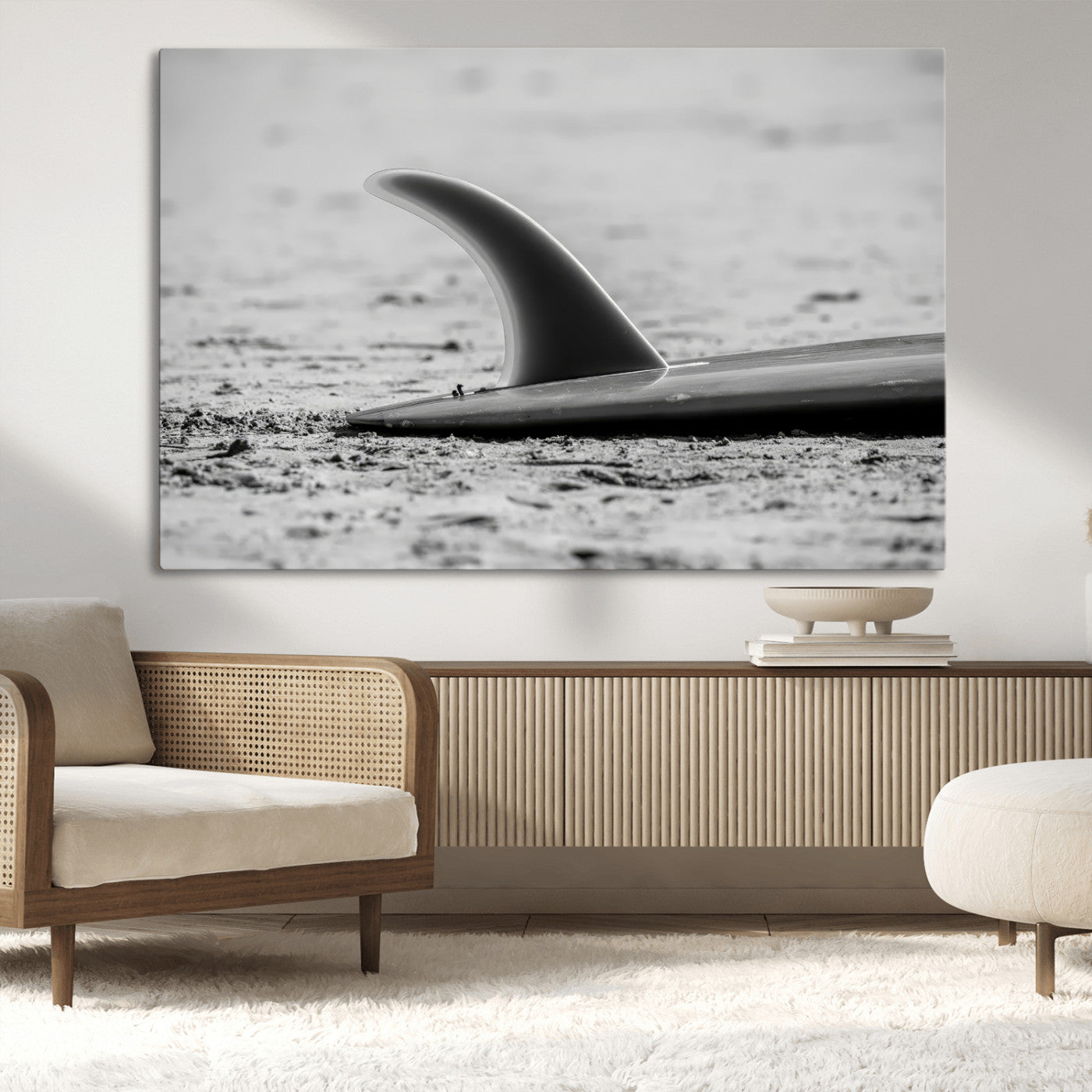 A black and white close-up of a surfboard fin resting on the sandy shore, highlighting minimalist beach aesthetics and classic surf culture.