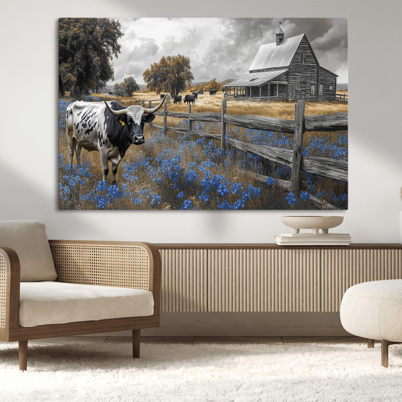 A Texas longhorn stands in front of a rustic barn and wooden fence, with bluebonnets and grazing cattle under dramatic skies.