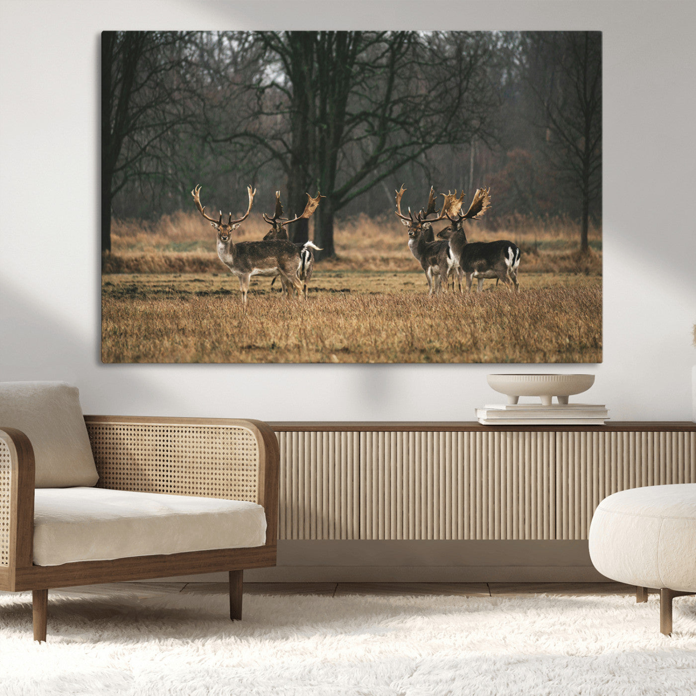 A group of majestic deer standing in a golden field with bare trees in the background, creating a peaceful woodland scene.