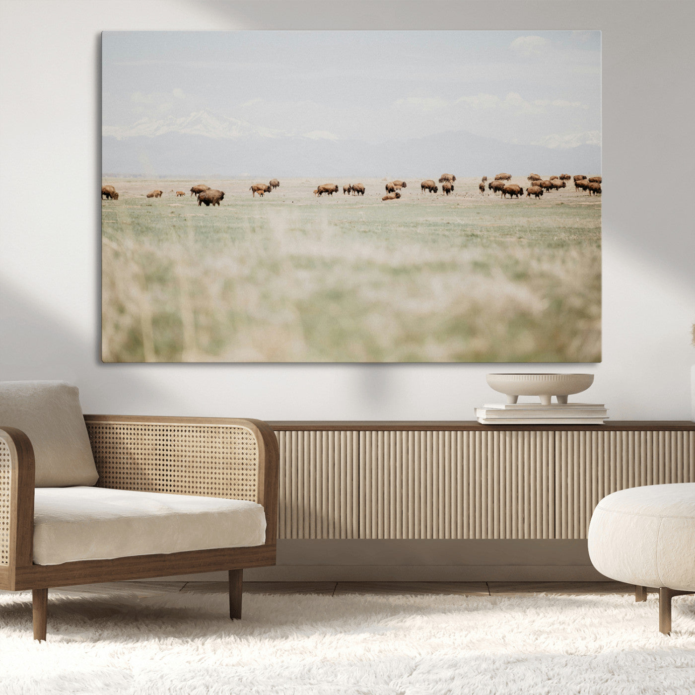 A herd of bison grazing in an open prairie with distant mountains under a soft sky, creating a serene and rustic Western landscape.