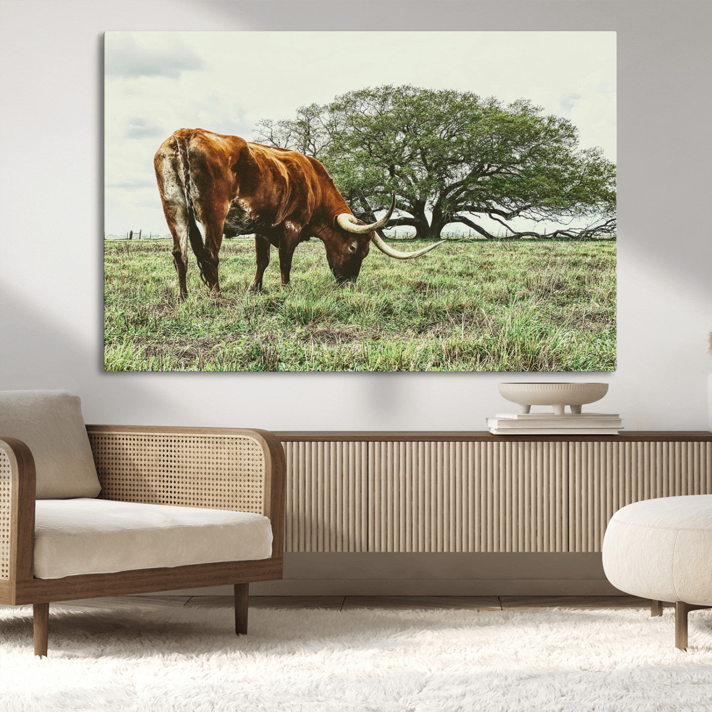 A Texas Longhorn grazing in a green pasture with a large tree in the background, evoking a rustic Western and farmhouse aesthetic.