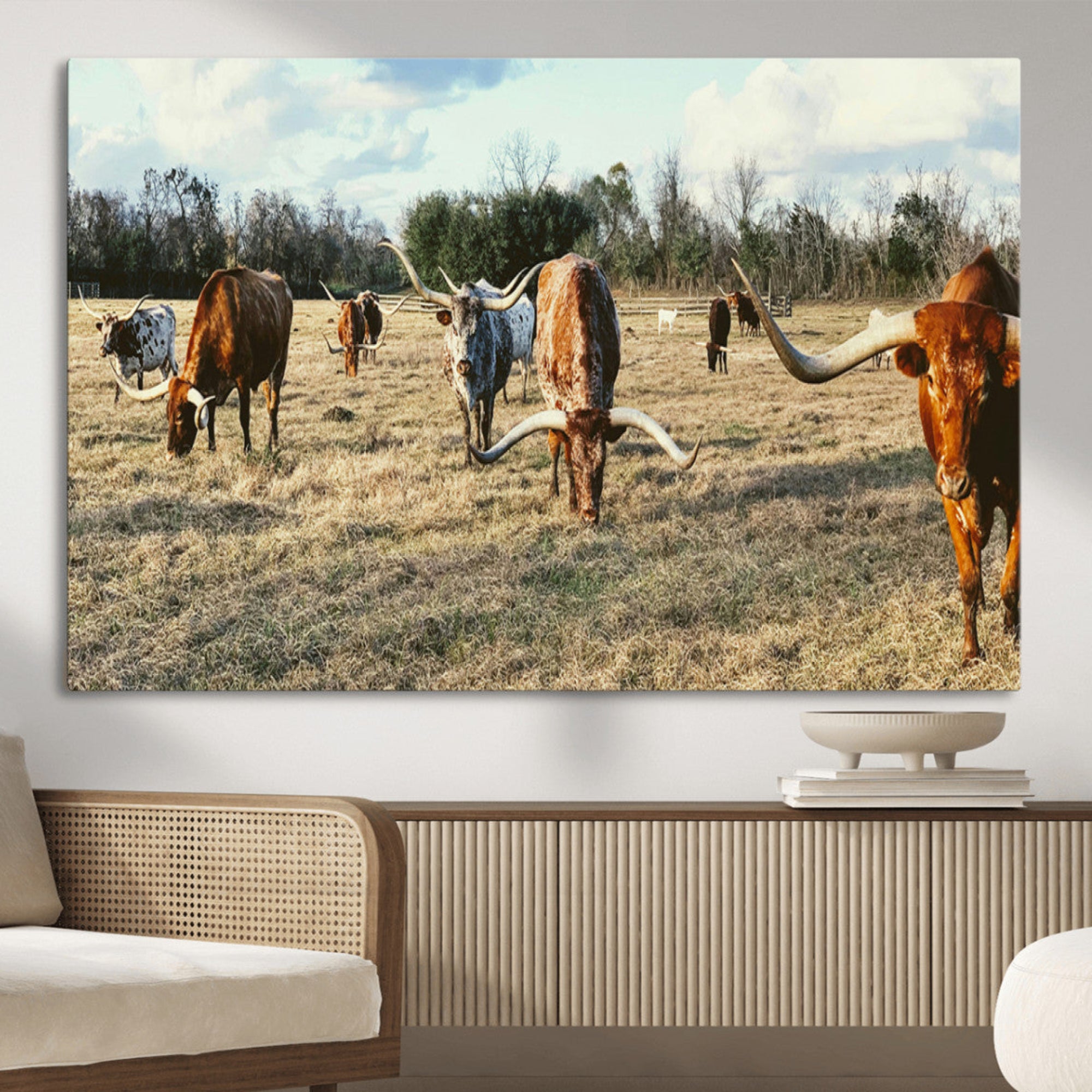 A herd of Texas Longhorn cattle grazing in an open field under a partly cloudy sky, capturing a rustic and Western ranch aesthetic.