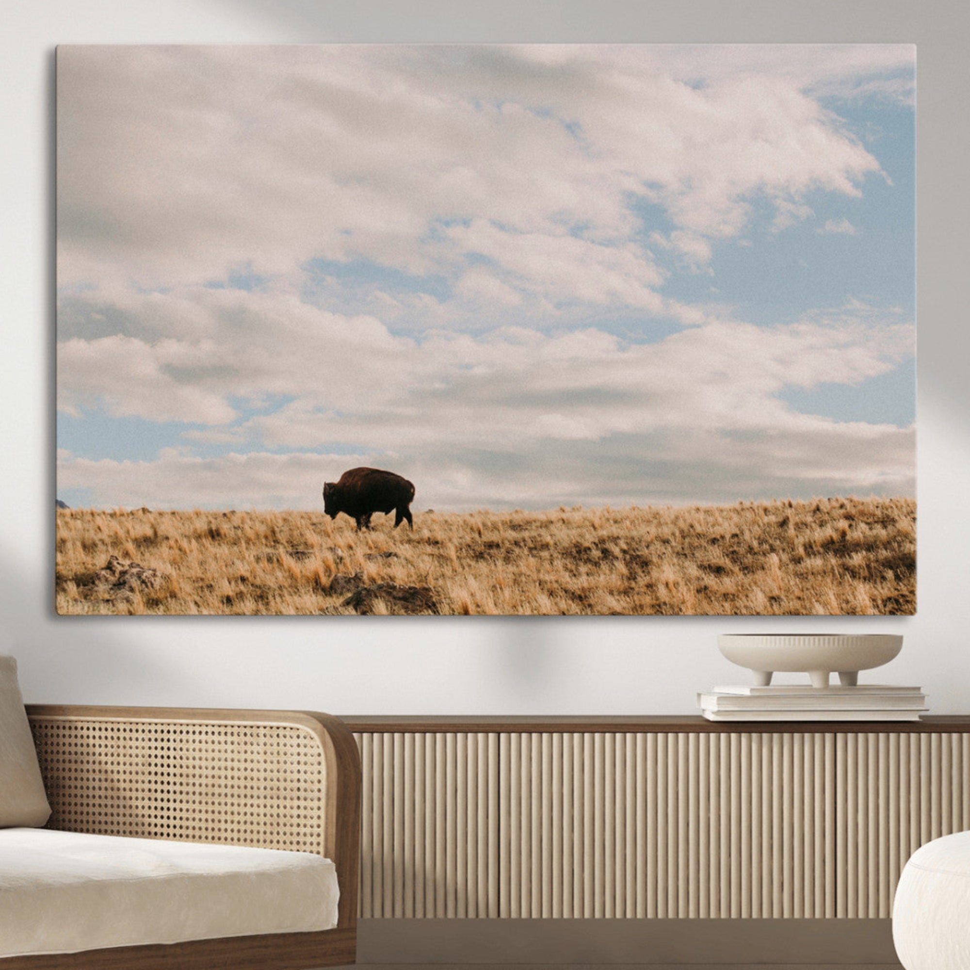 A solitary bison walking across a golden prairie under a vast, cloud-filled sky, evoking a peaceful, rustic western landscape for home decor.
