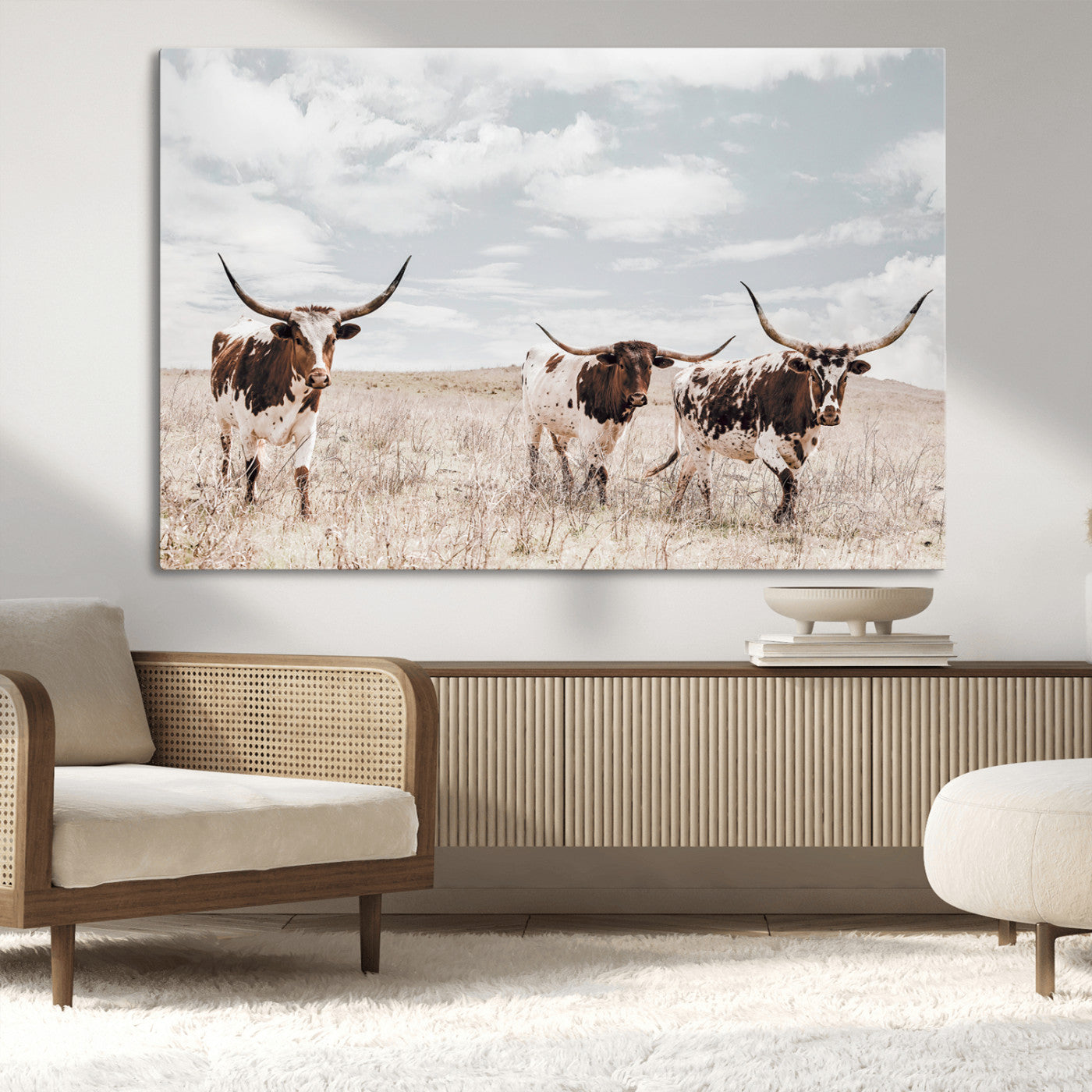 Three Texas Longhorn cattle walking through a dry grassy field under a partly cloudy sky.