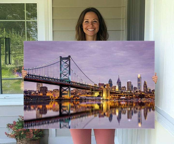 An Extra Large Wall Art Philadelphia Canvas Print, featuring a gallery-quality finish, captures the lit-up Ben Franklin Bridge and city buildings perfectly reflected on the water at sunset.