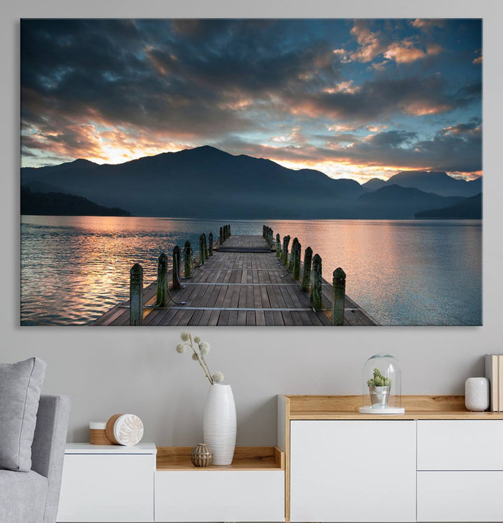 The Mountain Lake Wood Pier Canvas Wall Art depicts a serene lake and mountains, enhancing the beauty of any space.