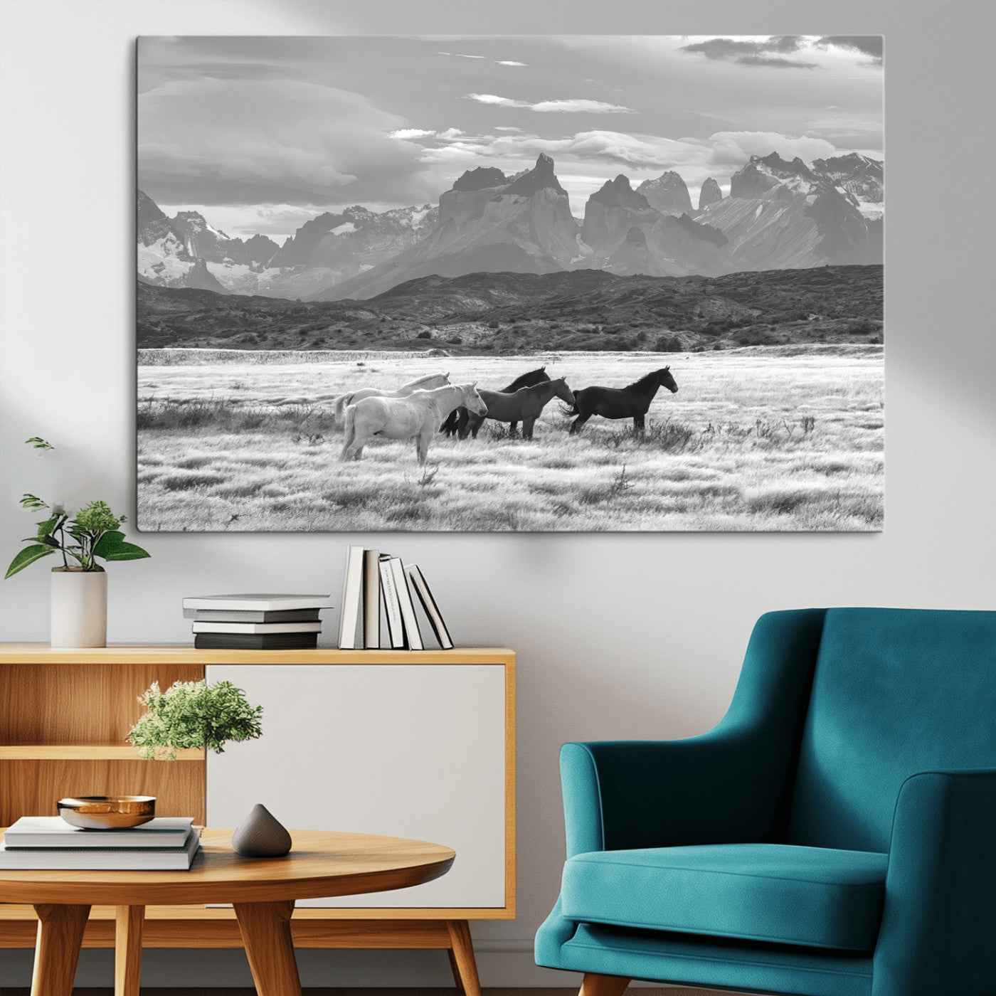 A black and white landscape of wild horses grazing in a vast grassland with towering mountains in the background, creating a moody and rustic western aesthetic.