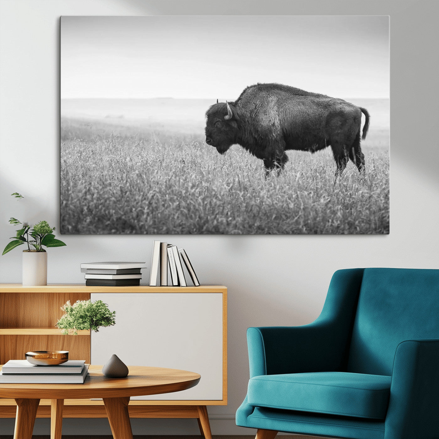 "Black and white image of a bison grazing in a vast field under an overcast sky."