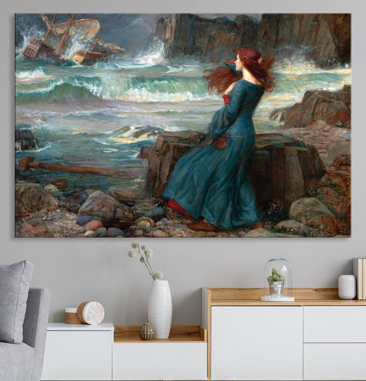 The Miranda by the Shore Wall Art Canvas Print depicts a woman in a blue dress standing by the sea, watching a shipwreck.