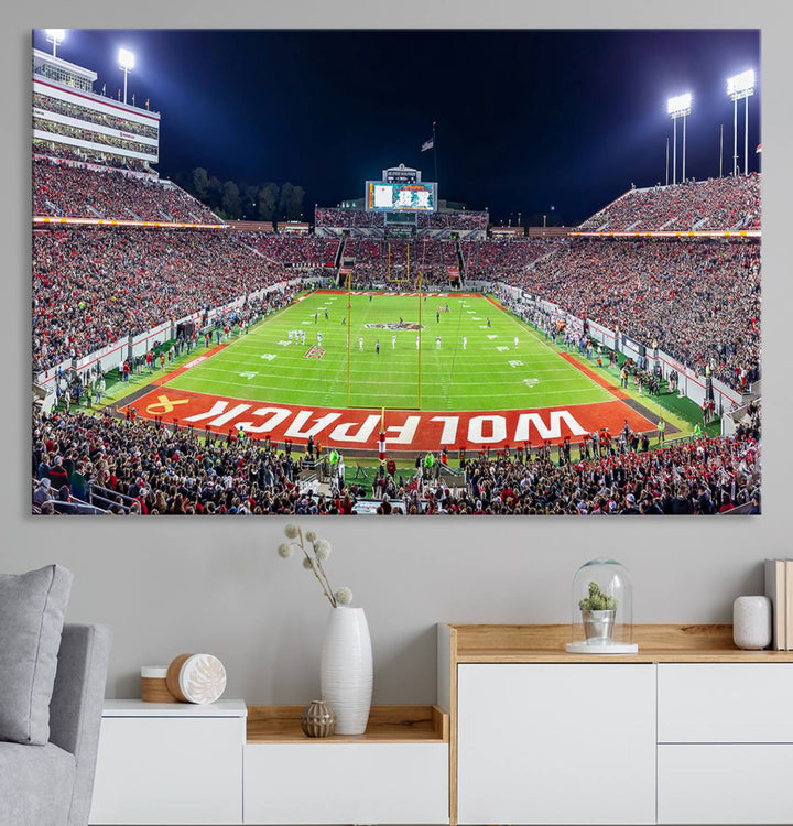 A NC State Wolfpack Football Team print of Carter-Finley Stadium at night features WOLFPACK illuminated brightly in the end zone grass.