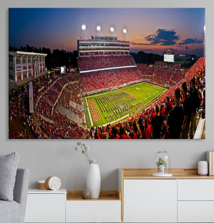 A print of a bustling Carter-Finley Stadium at dusk, featuring fans and a band, captures the essence of NC State Wolfpack football.