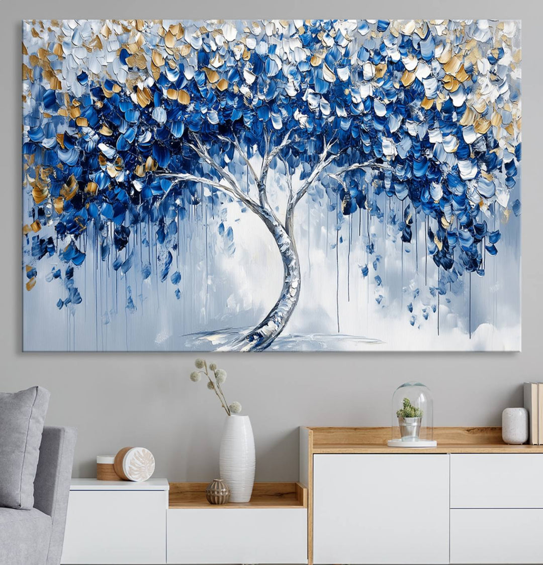 The Blue and Gold Abstract Tree Wall Art showcases a swirl trunk and features blue, silver, and gold leaves on a framed canvas print.