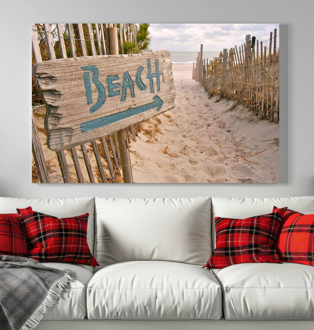 The Beach Is Calling You Wall Art Canvas Print features a sandy beach path with a wooden beach sign and arrow pointing to the ocean, beautifully displayed on museum-quality canvases.