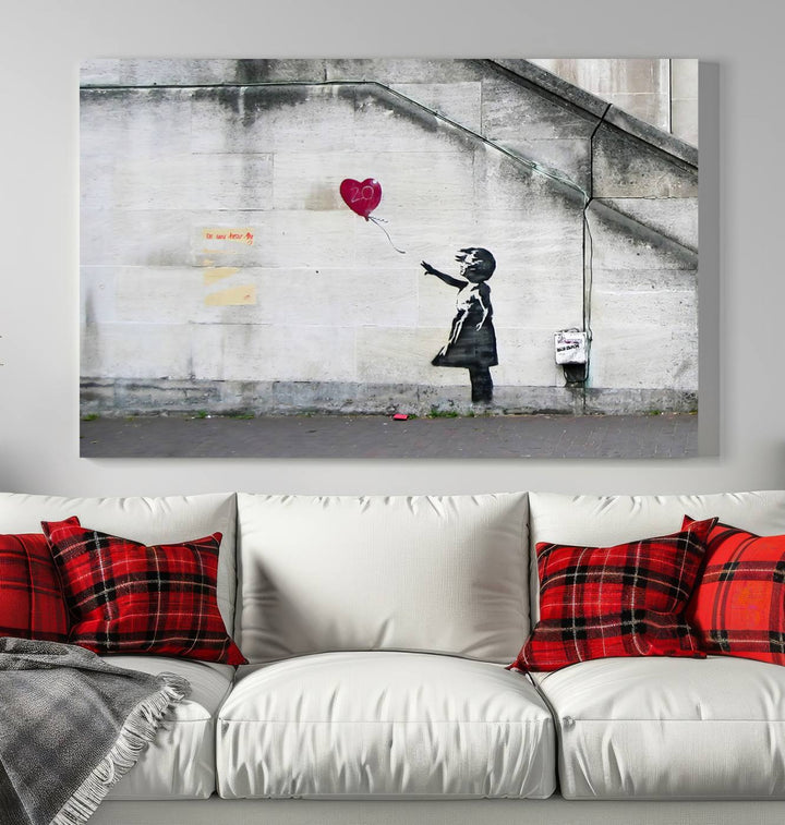 The "Girl with a Balloon Banksy Street Graffiti Art Canvas Print" is a gallery-quality wall art piece that features an image of a girl releasing a heart-shaped balloon. Handmade in the USA, this canvas artwork brings charm and emotion to any room.