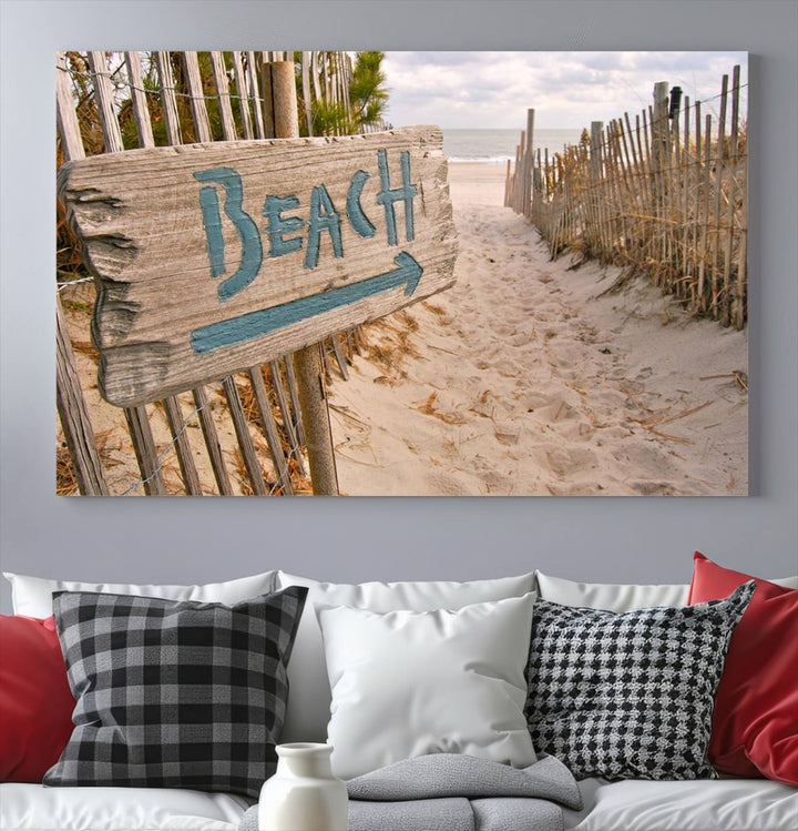 The Beach Is Calling You Wall Art Canvas Print features a sandy beach path with a wooden beach sign and arrow pointing to the ocean, beautifully displayed on museum-quality canvases.