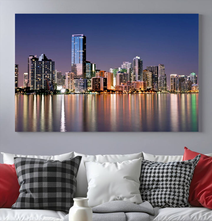 The Miami Skyline Canvas Wall Art Print showcases a vibrant night cityscape and beautifully captures the dazzling colorful lights reflecting on the water. This ready-to-hang triptych adorns the wall, creating a stunning visual centerpiece.