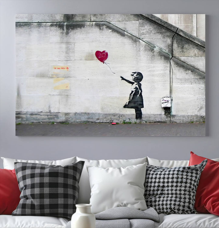 The "Girl with a Balloon Banksy Street Graffiti Art Canvas Print" is a gallery-quality wall art piece that features an image of a girl releasing a heart-shaped balloon. Handmade in the USA, this canvas artwork brings charm and emotion to any room.