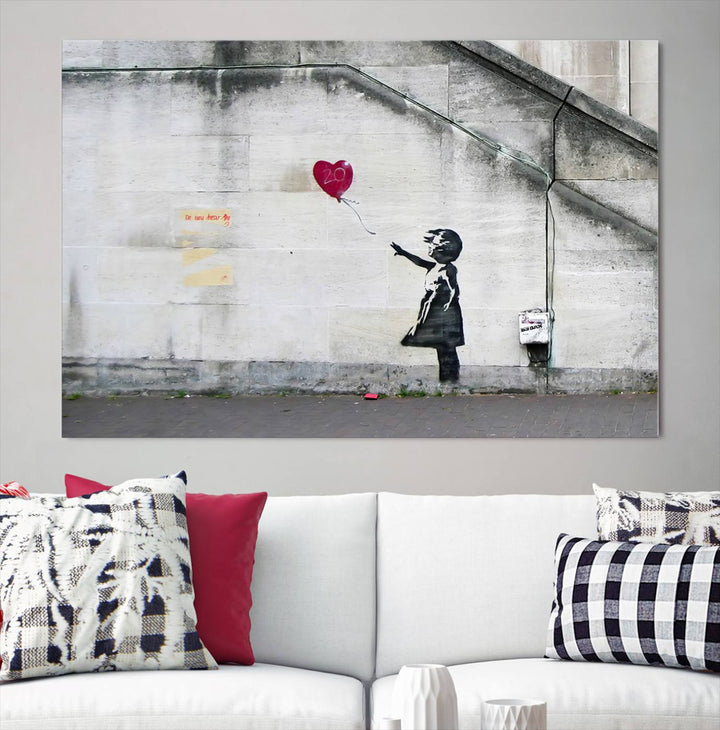 The "Girl with a Balloon Banksy Street Graffiti Art Canvas Print" is a gallery-quality wall art piece that features an image of a girl releasing a heart-shaped balloon. Handmade in the USA, this canvas artwork brings charm and emotion to any room.