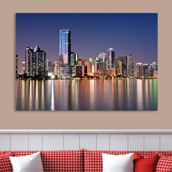 The Miami Skyline Canvas Wall Art Print showcases a vibrant night cityscape and beautifully captures the dazzling colorful lights reflecting on the water. This ready-to-hang triptych adorns the wall, creating a stunning visual centerpiece.