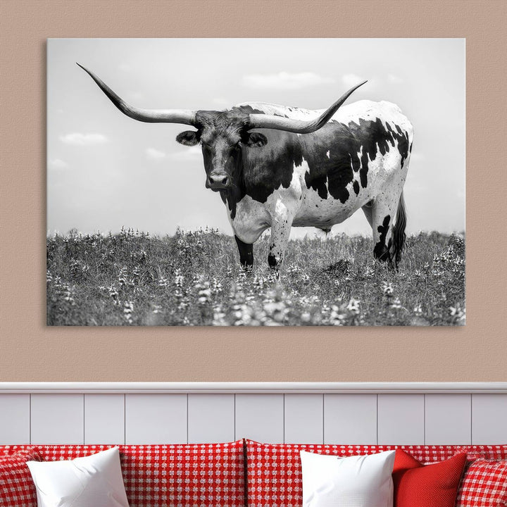 The Texas Black White Highland Longhorn Cow Wall Art Canvas Print, a gallery-quality triptych, elegantly adorns the wall, showcasing a striking black-and-white depiction of a longhorn cow in a field.