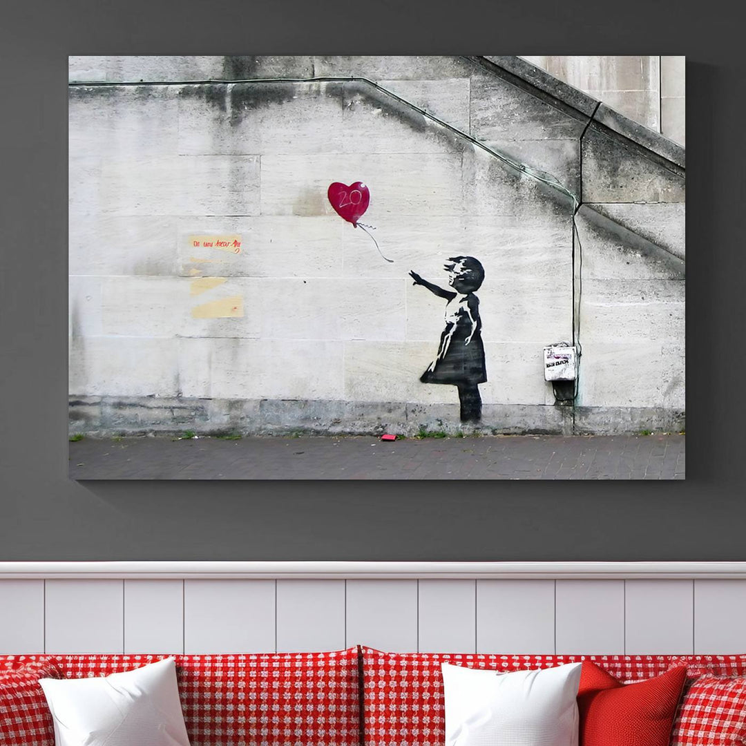 The "Girl with a Balloon Banksy Street Graffiti Art Canvas Print" is a gallery-quality wall art piece that features an image of a girl releasing a heart-shaped balloon. Handmade in the USA, this canvas artwork brings charm and emotion to any room.