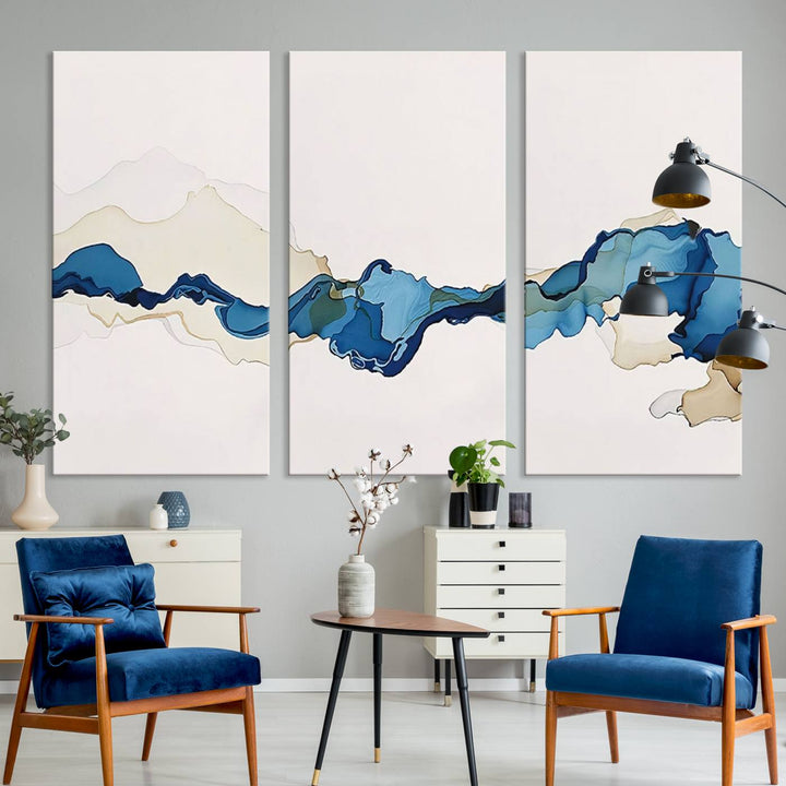 The modern living room showcases a set of three canvas prints with abstract blue art on museum-quality materials.