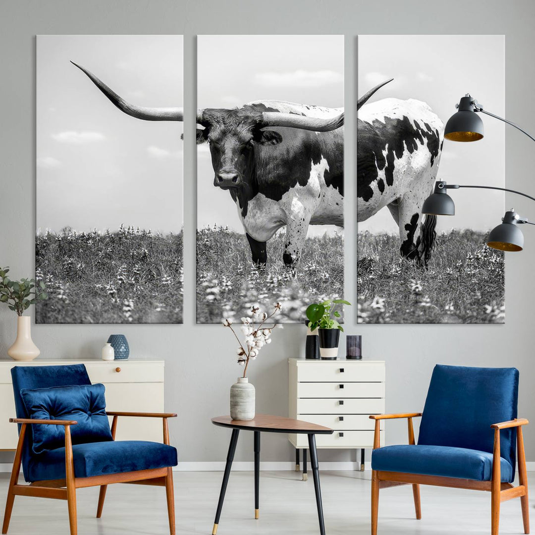 The Texas Black White Highland Longhorn Cow Wall Art Canvas Print, a gallery-quality triptych, elegantly adorns the wall, showcasing a striking black-and-white depiction of a longhorn cow in a field.