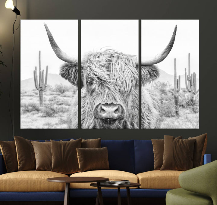 The "Rustic Charm | Cow Longhorn Black White Bighorn Wall Art Canvas Print" is a stunning triptych that showcases a highland cow with long horns set against a desert landscape with cacti in the background. This farmhouse wall art elevates any room into a rustic haven with its gallery-quality canvas.