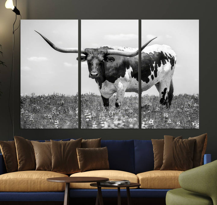 The Texas Black White Highland Longhorn Cow Wall Art Canvas Print, a gallery-quality triptych, elegantly adorns the wall, showcasing a striking black-and-white depiction of a longhorn cow in a field.