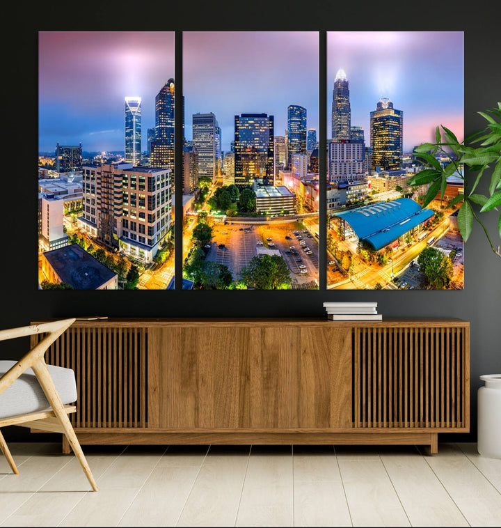 The living room features three large pieces of the *Charlotte City Lights Sunset Purple Skyline Cityscape View Wall Art Canvas Print*. Crafted on gallery-wrapped, museum-quality canvas with UV-protective coating, they grace the wall and add an artistic flair to the space.